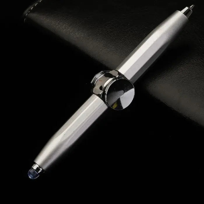 Silver fidget spinner pen and stylus combo displayed on a black leather surface.