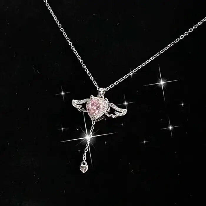 Silver heart pendant necklace with pink gemstone and wing design, shown on a sparkling black background.