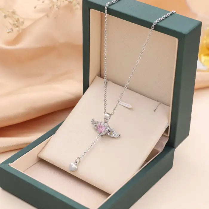 Silver heart pendant necklace with pink gemstone and wing design, elegantly presented in a green box.