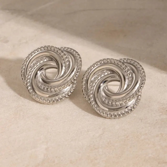 Shiny silver twisted knot earrings on a beige background, ideal for adding elegance to everyday looks.