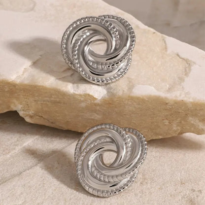 Intricate silver knot earrings resting on a stone surface, showcasing elegant and sophisticated craftsmanship.