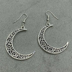 Intricately designed silver crescent moon earrings displayed on a soft fabric background.