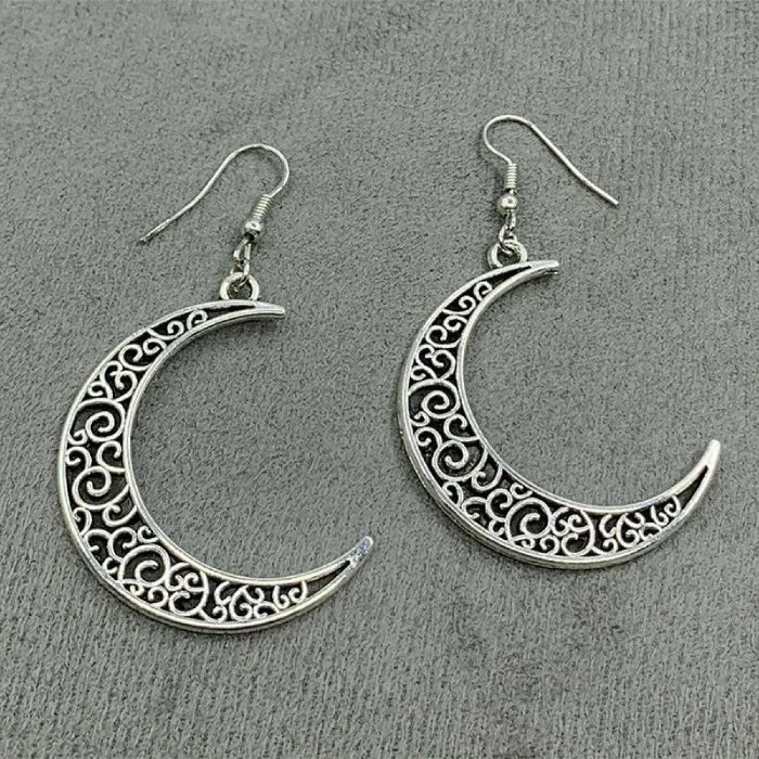 Intricately designed silver crescent moon earrings displayed on a soft fabric background.