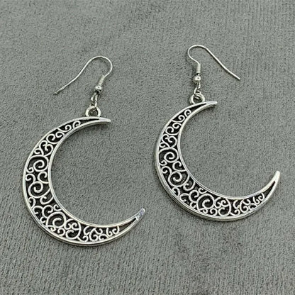 Intricately designed silver crescent moon earrings displayed on a soft fabric background.