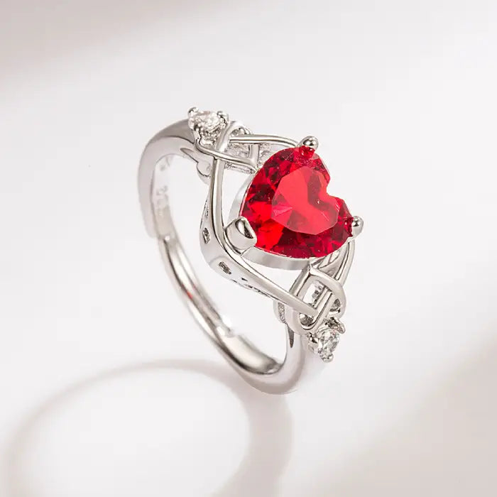 Stunning silver ring with a heart-shaped red gemstone and intricate intertwined design.