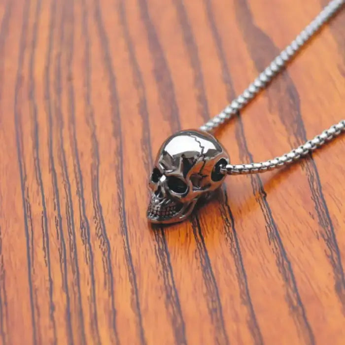 Stylish silver skull necklace resting on a wooden surface, showcasing fine metallic details.