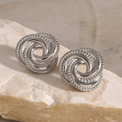 Polished silver twisted knot earrings on white stone, a sleek and timeless addition to any jewelry collection.