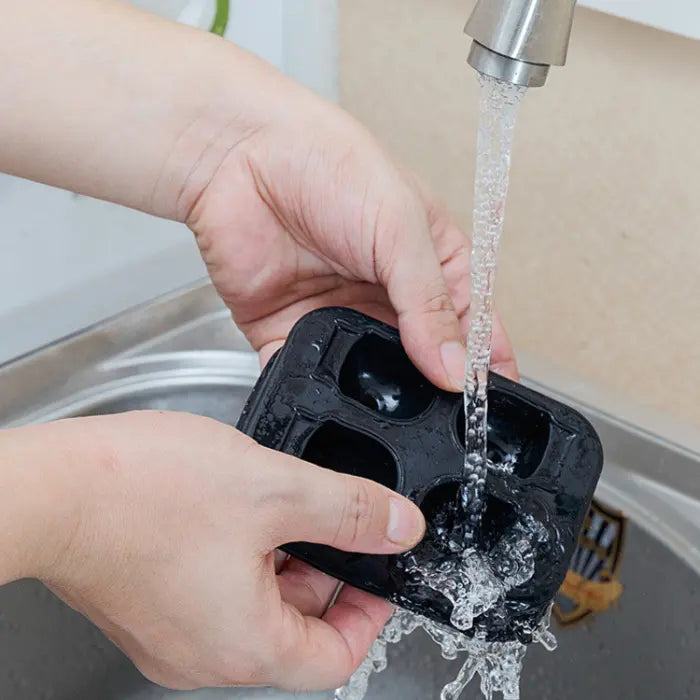 Skull ice cube mold being washed under faucet with hands holding flexible tray under water.