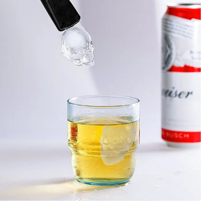 Skull ice cube dropped into whiskey glass with visible skull shape floating in drink.