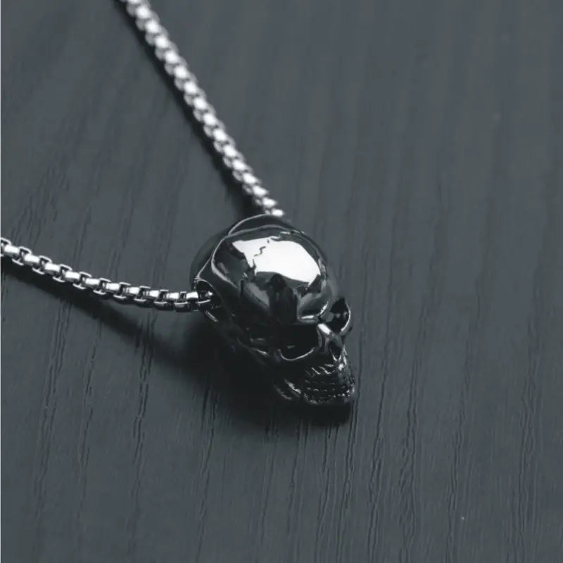 Silver skull necklace displayed on a dark wooden surface for a bold and edgy aesthetic.