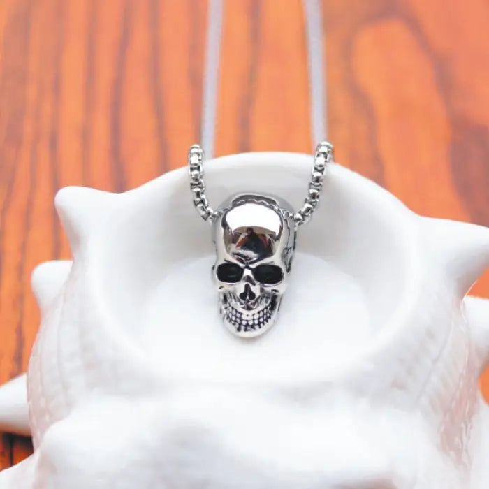 Silver skull necklace displayed in a decorative white bowl, highlighting its intricate design.