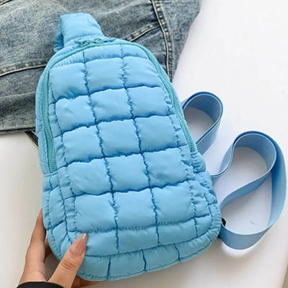 Sky blue puffer crossbody bag with quilted design and adjustable strap, shown against denim jacket backdrop