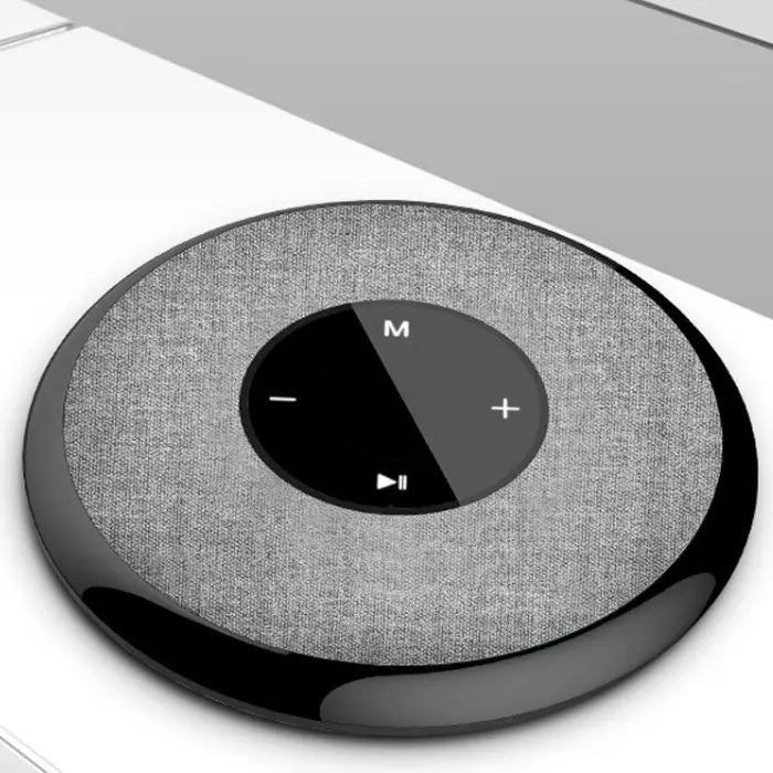 Angled view of circular smart speaker with fabric cover and touch controls, placed on a white surface