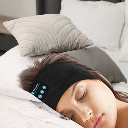 Woman sleeping with Bluetooth headband headphones on a cozy bed featuring soft pillows.