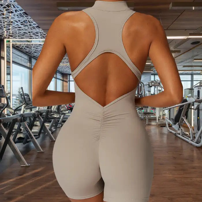 sleeveless yoga bodysuit in neutral beige with distinctive diamond-shaped open back and ruched bottom detail for enhanced mobility