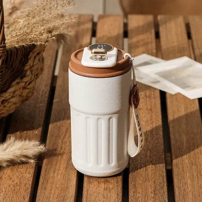 White smart thermos with digital temperature display on wooden surface, surrounded by wheat stems and woven basket