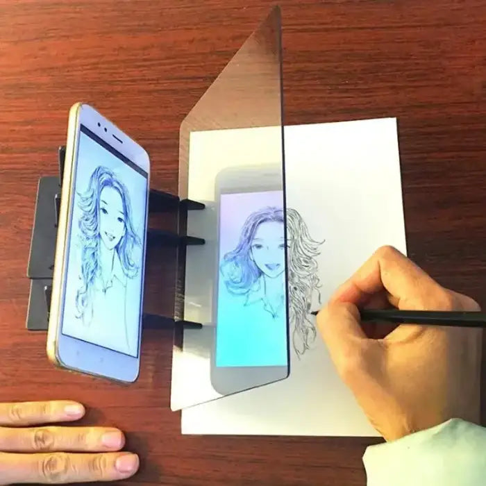 Hand drawing portrait on paper using smartphone projection device with folding mirror panel on wooden surface