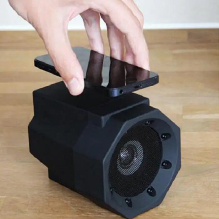 Hand placing smartphone on black octagonal wireless induction speaker on wooden surface