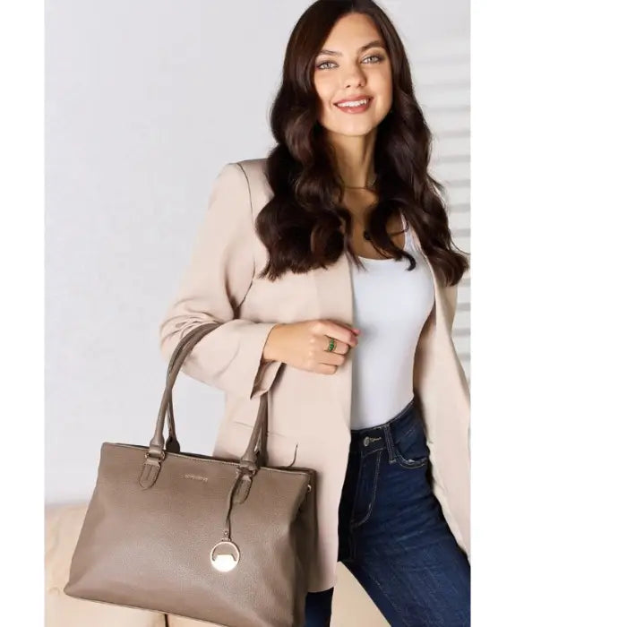 Smiling woman in a beige blazer holding a gray leather bag.