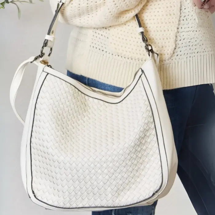  Cheerful woman with blonde hair showcasing a white textured shoulder bag, indoor setting.