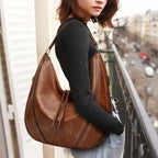 Soft leather hobo bag with perforated detail in brown worn on shoulder, lifestyle view on model with city backdrop.