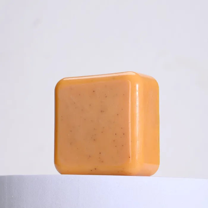 Soft orange handmade soap bar with textured exfoliants on white base.