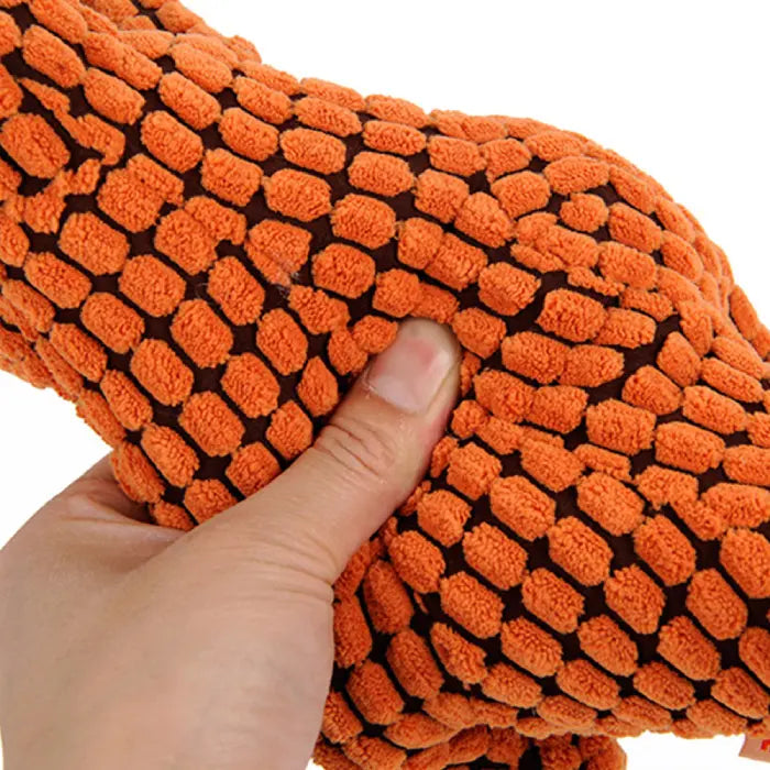 A hand squeezing the soft, textured orange plush dinosaur dog toy, showing its flexible design.