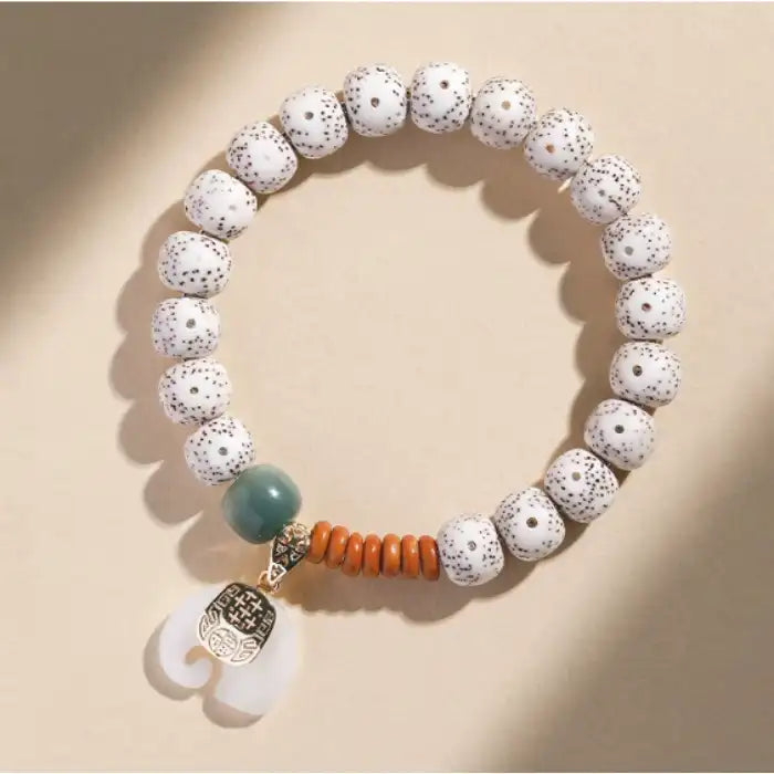  Flat lay of speckled ceramic bead bracelet with elephant charm, displaying white speckled beads and charm pendant.