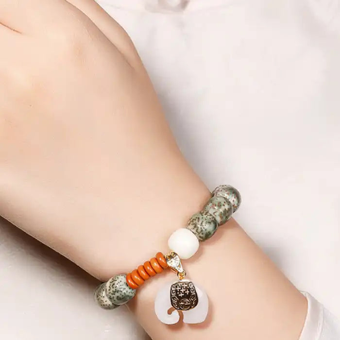 Speckled ceramic bead bracelet with elephant charm, worn on wrist with orange accent beads and green stone detail.