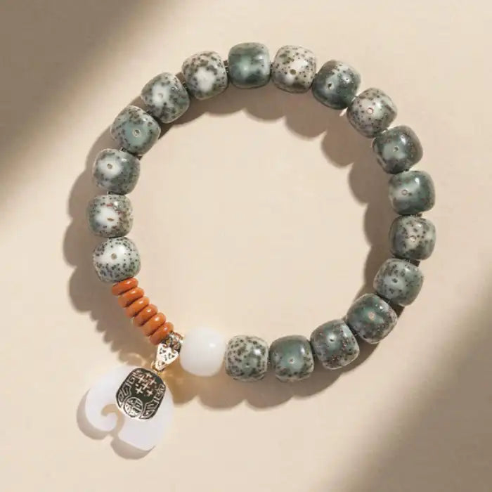  Overhead view of speckled ceramic bead bracelet with elephant charm, featuring green beads and orange accents.