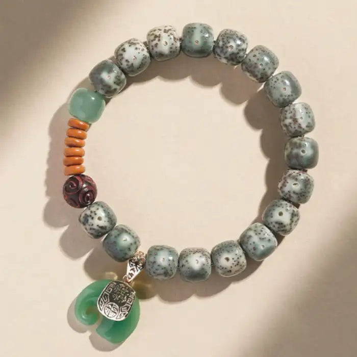  Side angle of speckled ceramic bead bracelet with elephant charm, showing green jade pendant and decorative beads.
