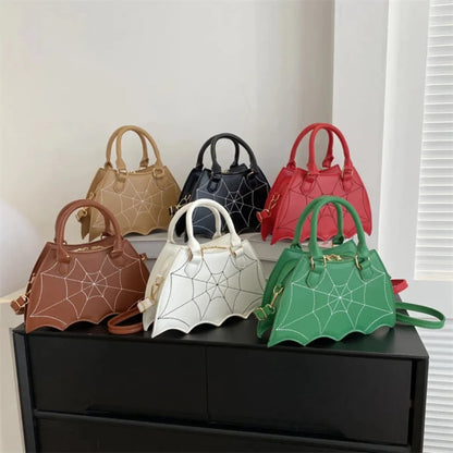 Six bat-wing shaped handbags with spiderweb designs in various colors displayed on black dresser against white wall