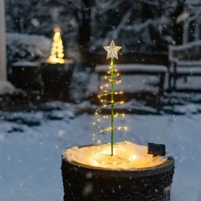 Spiral Christmas tree with warm LED lights on a tree stump, illuminating a snowy backyard during snowfall