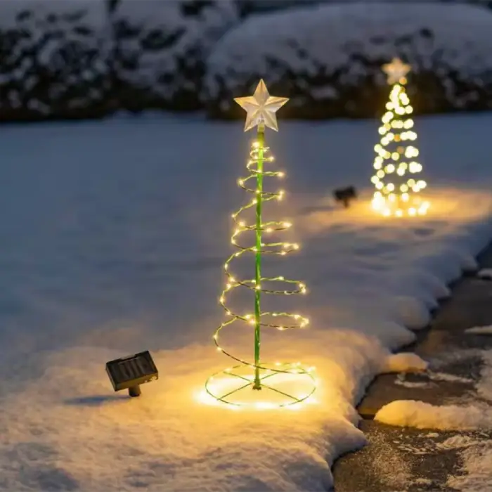 Spiral Christmas tree with warm LED lights casting a golden glow on snow, solar panel visible nearby