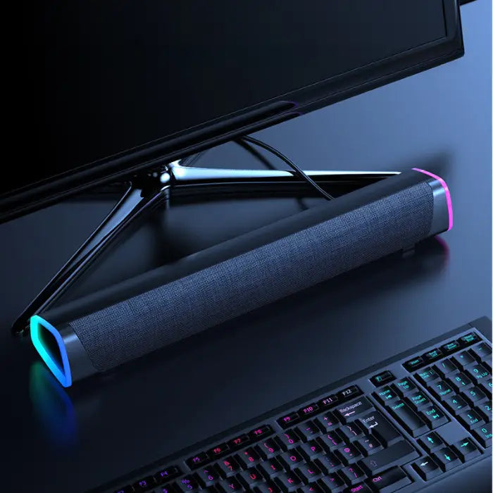 Black soundbar with pink LED accent, wired connection, positioned in front of a computer screen and gaming keyboard