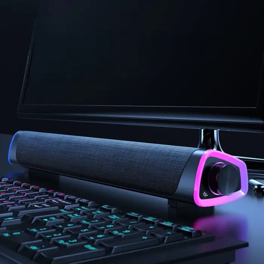 Slim soundbar with colorful LED accents positioned under a computer monitor, next to a gaming keyboard