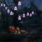 String lights featuring ghosts hanging on a tree near pumpkins and a haunted house.