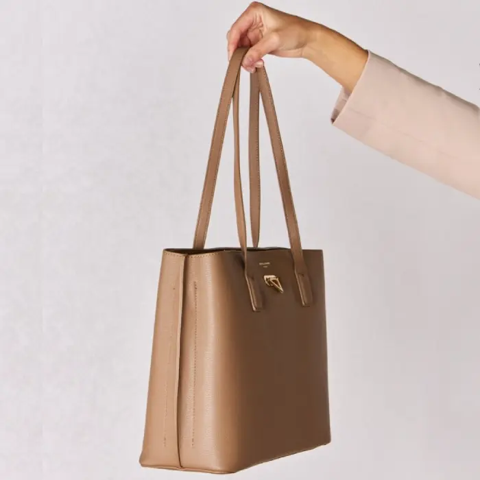 Side view of a tan leather tote bag held by a hand, showing its depth and sturdy construction