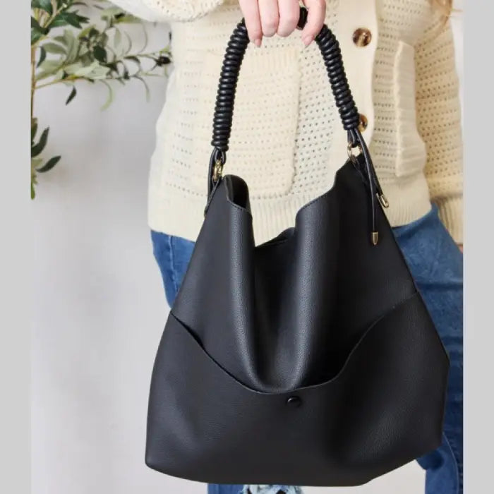 Stylish black handbag with coiled handle held by woman in cream cardigan