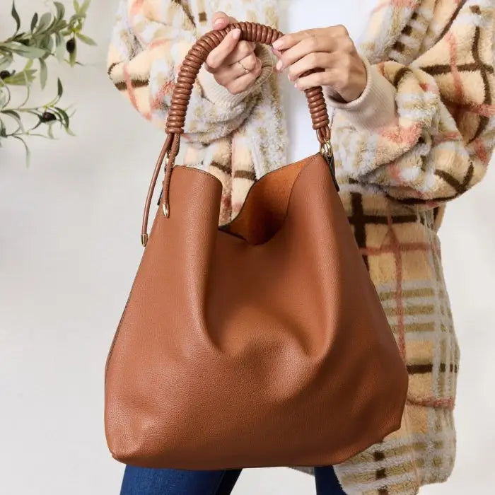 Stylish brown handbag with coiled handle held by woman in plaid jacket