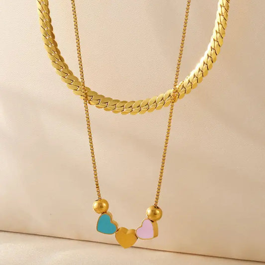 Gold necklaces with heart-shaped pendants in blue, yellow, and pink laid elegantly on a cream-colored fabric.