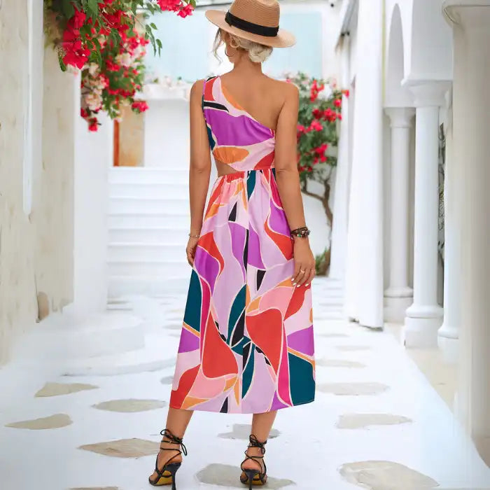 Summer dress showcasing back view of one-shoulder cutout design with bold geometric print pattern against whitewashed Mediterranean backdrop