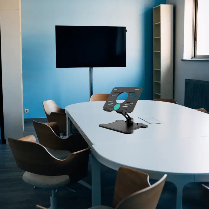 Tablet stand placed on long boardroom table in modern conference room with wood and glass decor.