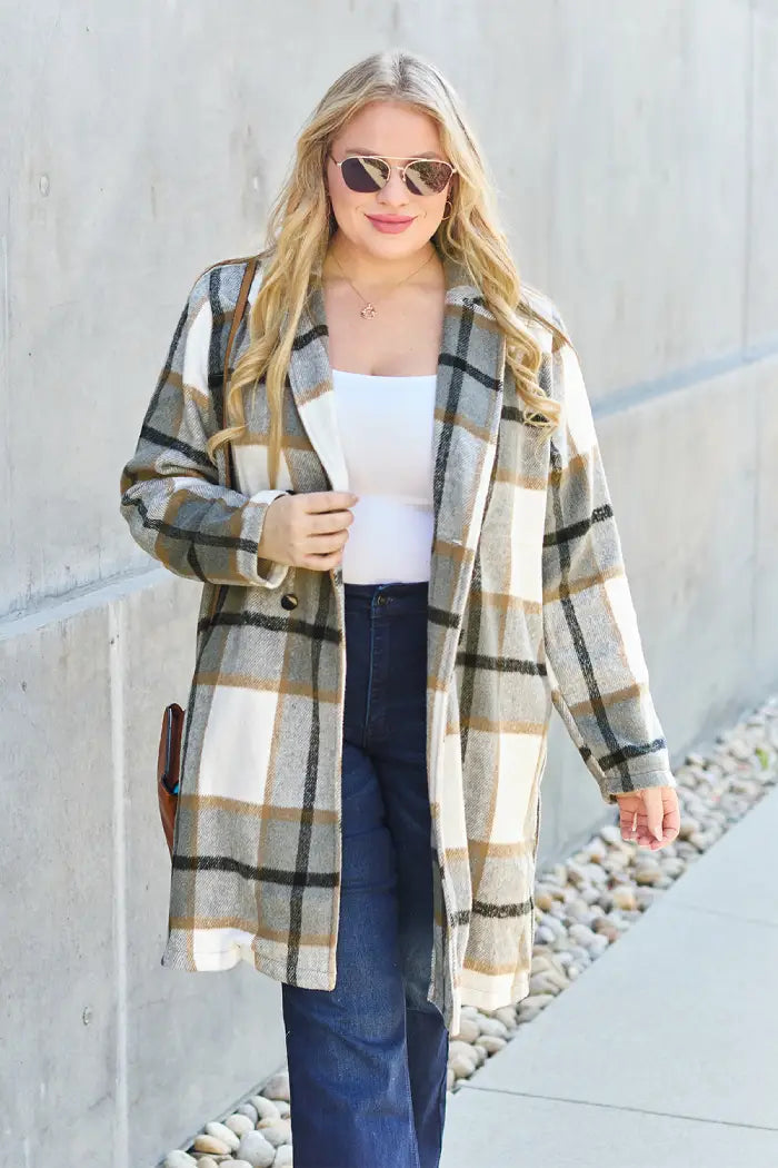 Woman wearing a tan and white plaid wool coat styled with a white top, dark jeans, and a crossbody bag in an outdoor setting.