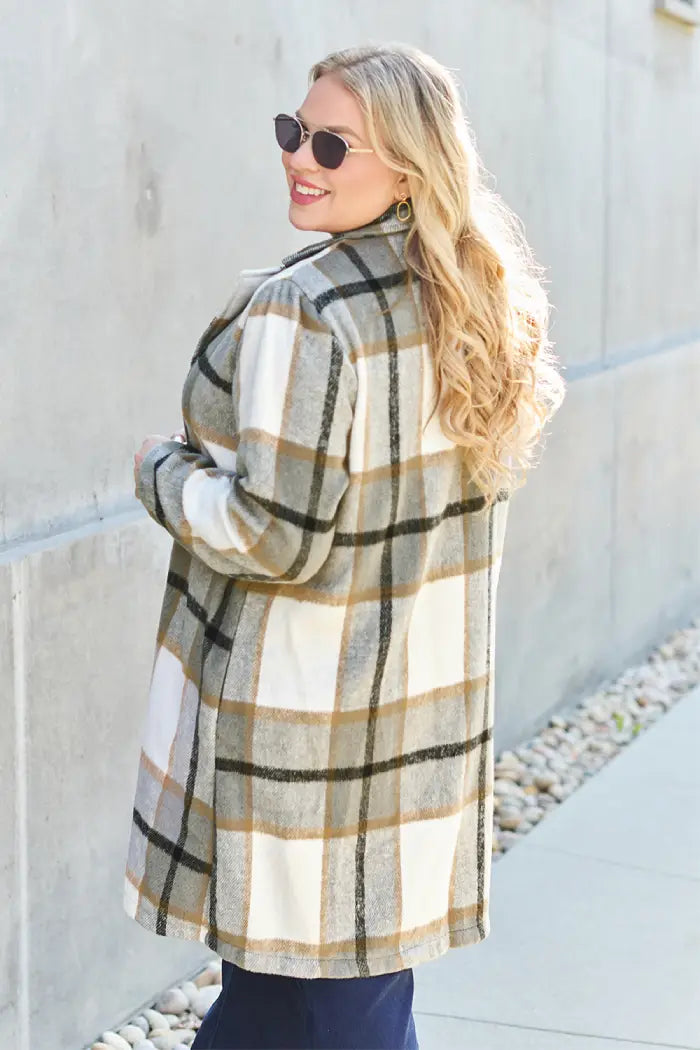 Plus-size woman in a tan and white plaid wool coat, showing the back view, styled with dark jeans and sunglasses.