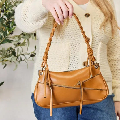 Styled shot of camel leather handbag paired with cream knit cardigan, showing decorative zipper details and braided strap