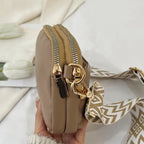 Taupe crossbody bag with gold-tone zippers and a chevron strap, showcasing a sleek and compact design.