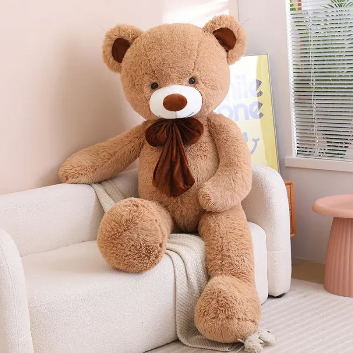 Giant gray teddy bear with a dark bow, seated in a modern living room.