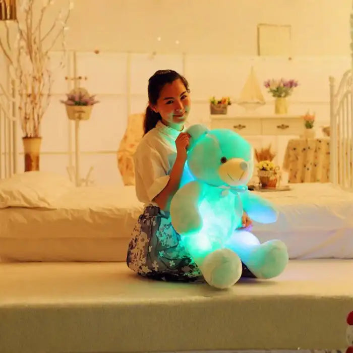 Teddy Bear glowing blue plush held by a woman on a bed.