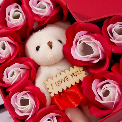 Close-up of teddy bear surrounded by red and pink artificial roses in a heart-shaped gift box.